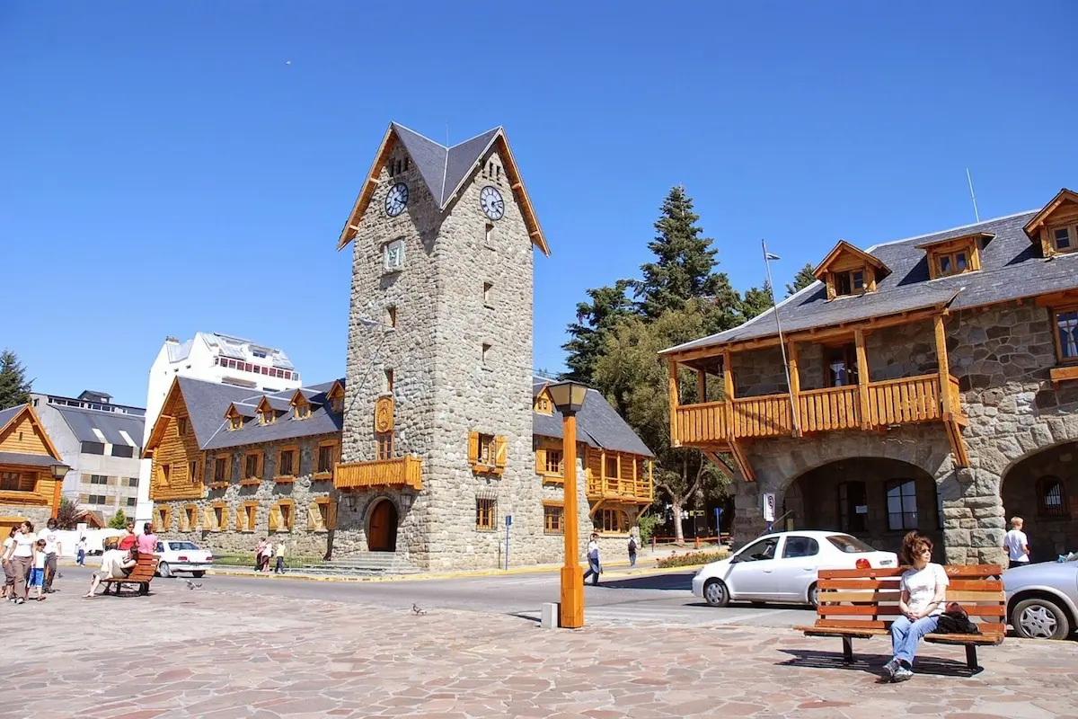 Het iconische stenen stadhuis op het Centro Cívico plein in Bariloche met op de achtergrond het blauwe Nahuel Huapi-meer.