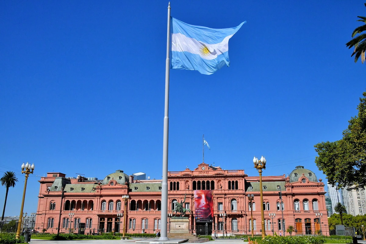 Het roze presidentiële paleis Casa Rosada aan de Plaza de Mayo onder een strakblauwe lucht met de Argentijnse vlag prominent in beeld.