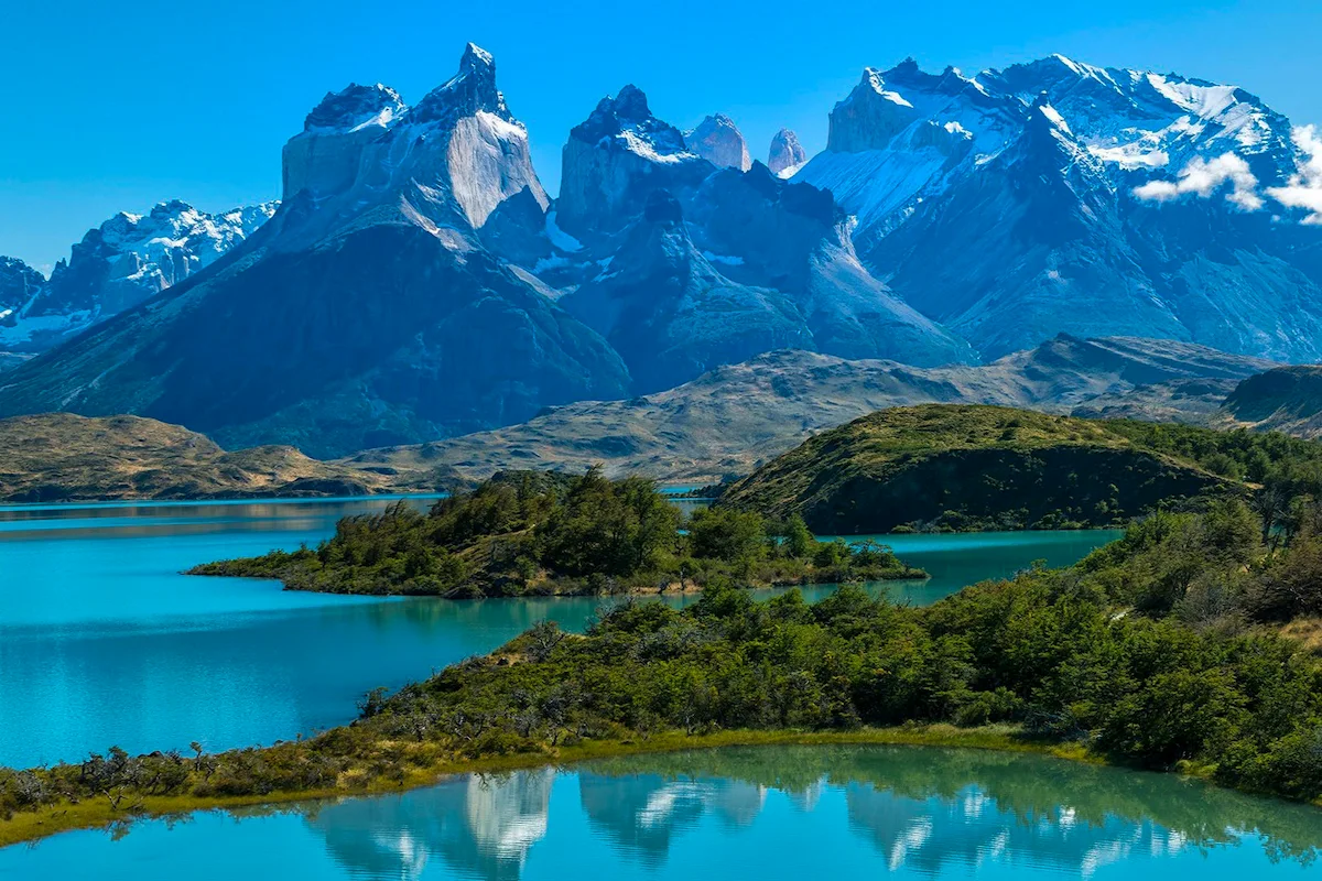Een panoramisch uitzicht over de tweekleurige granieten Cuernos del Paine en de besneeuwde Paine Grande weerspiegeld in het melkblauwe Lago Pehoé in het Nationaal Park Torres del Paine, Chili.