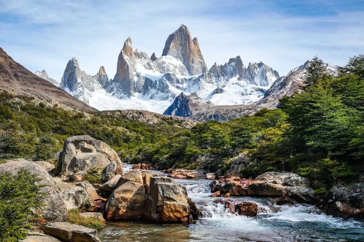 Uitzicht op de iconische granieten pieken van het Fitz Roy-massief met sneeuw en gletsjers boven een stromende rivier in El Chaltén.