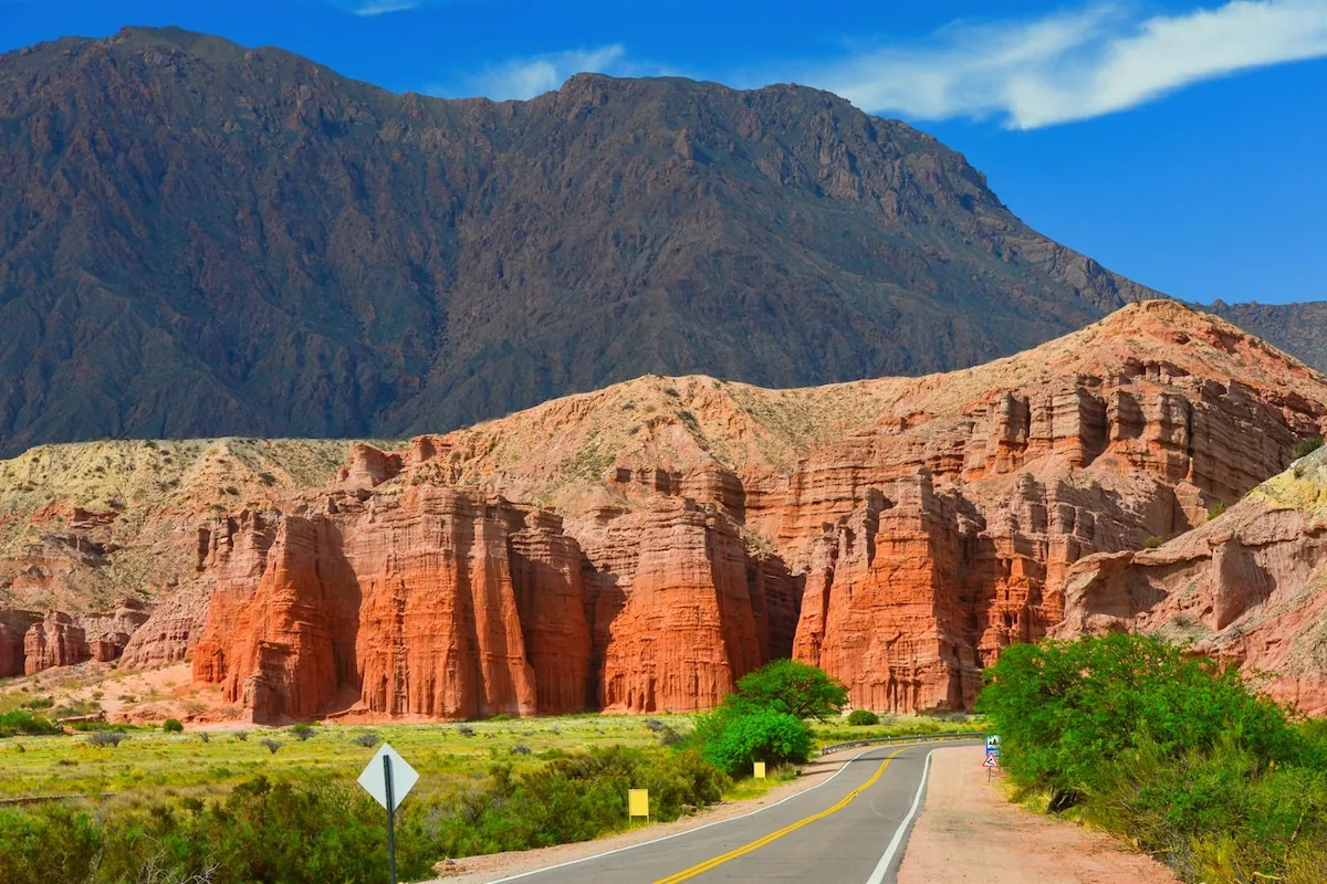 Een auto rijdt op de Ruta 68 langs de indrukwekkende, torenhoge rode rotsformaties van 'Los Castillos' in de Quebrada de las Conchas nabij Cafayate.