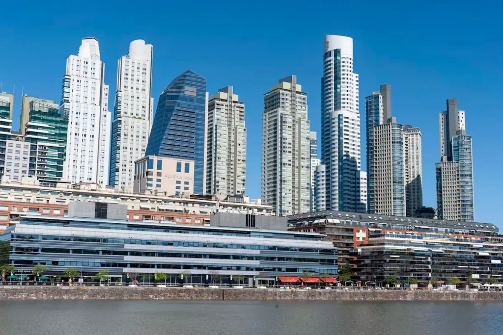 Een uitzicht over het water op de moderne wolkenkrabbers en luxe appartementencomplexen van de wijk Puerto Madero in Buenos Aires onder een strakblauwe lucht.