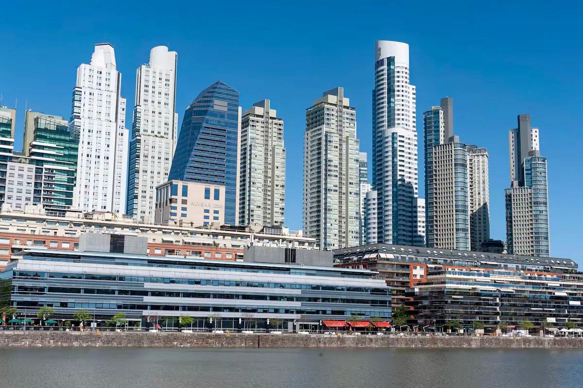 Een uitzicht over het water op de moderne wolkenkrabbers en luxe appartementencomplexen van de wijk Puerto Madero in Buenos Aires onder een strakblauwe lucht.