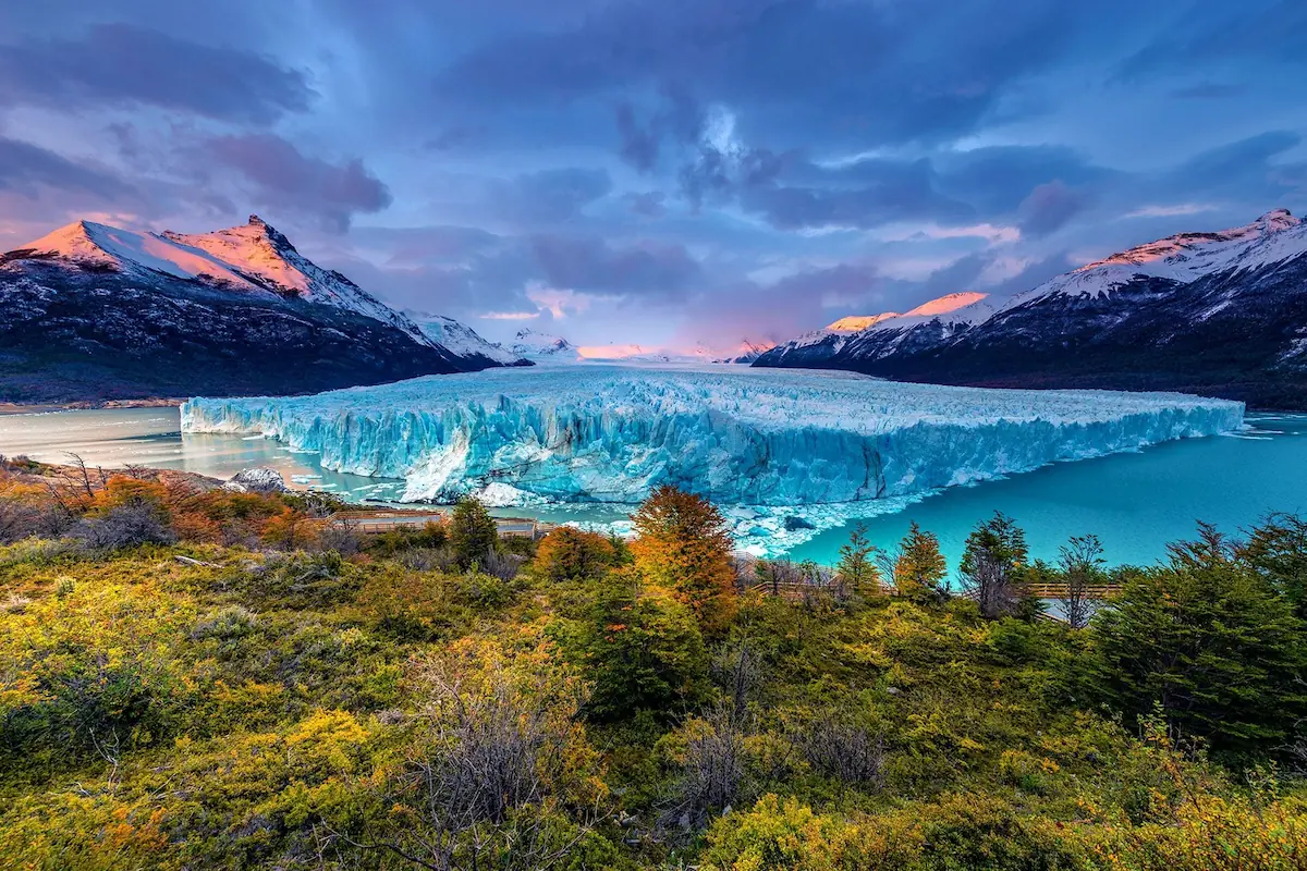 Panoramisch uitzicht op de enorme ijsmuur van de Perito Moreno-gletsjer in El Calafate, omgeven door besneeuwde Andes-toppen en herfstkleuren.
