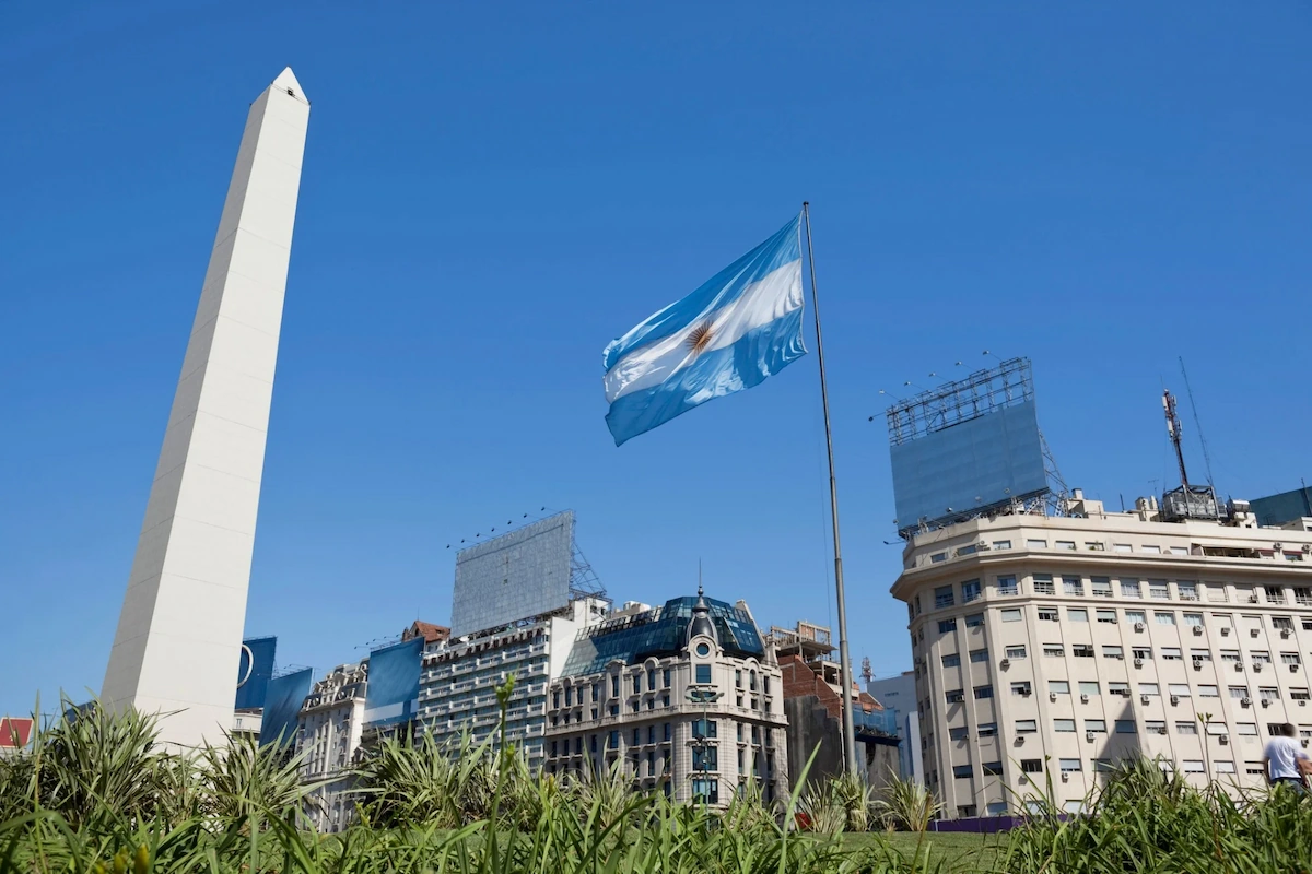 De nationale vlag van Argentinië wappert fier naast de witte Obelisk in Buenos Aires onder een strakblauwe lucht.
