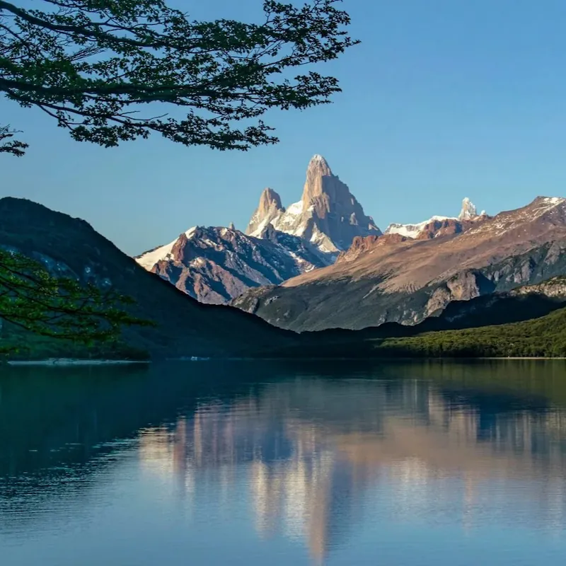 De iconische bergtop van de Fitz Roy weerspiegelt in het heldere water van Laguna del Desierto, omgeven door dichte bossen en bergen.
