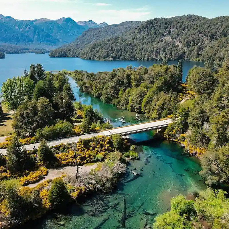 Een luchtfoto van de brug over de heldere, turquoise Río Ruca Malen, omgeven door dichte bossen en bergen langs de Zeven Meren Route.