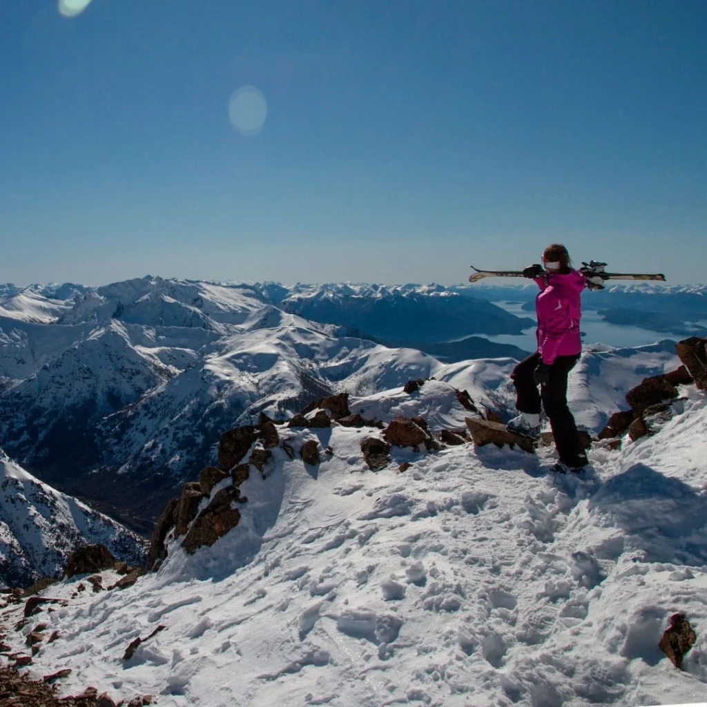 Een skiër met ski's op de schouder geniet van het uitzicht op de besneeuwde Andes vanaf Cerro Catedral in Bariloche.